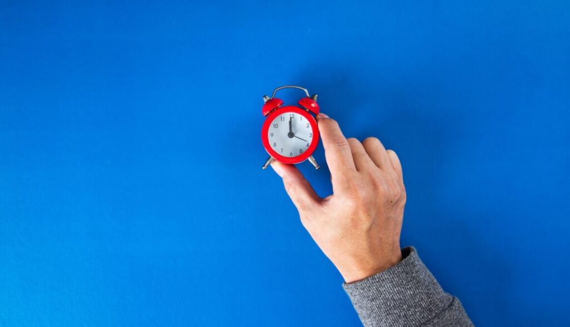 Time optimization concept. hand holding alarm clock on blue background.